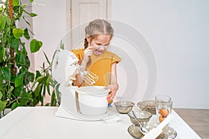 kid girl prepares dough in submersible mixer, tries and it tastes unpalatable