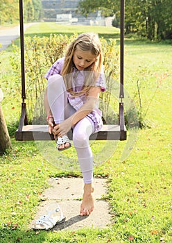 Kid - girl putting on shoes on swing