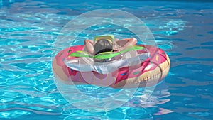 Kid girl relaxing on inflatable rings in swimming pool summer day, rear view