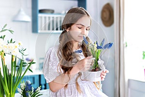 Kid girl sit on kitchen with spring flowers. Happy little girl in dress with ponytails hair holding bouquet flowers. photo