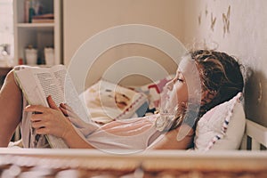 Kid girl sitting on bed and reading book in her room. Cozy weekend at home