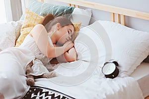 Kid girl sleeping in early morning in bed with alarm clock