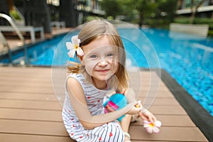 Kid girl smile at camera sitting close to swimming pool wearing