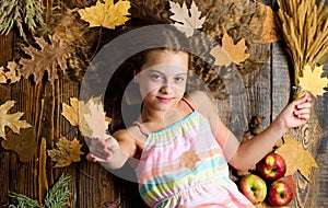 Kid girl smiling face relax wooden background autumn attributes top view. Child with long hair with autumn maple leaves