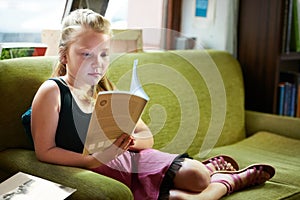 Kid, girl on sofa and reading book for home learning, education and story with knowledge or creative mind. Child relax