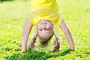 Kid girl standing upside down on her head on grass in summer