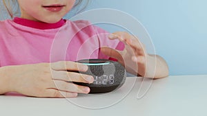 Kid girl talking to smart speaker and give it orders Little child using smart speaker at home while doing homework.