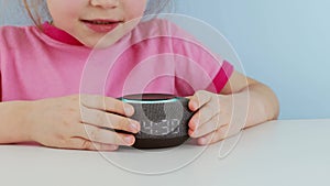 Kid girl talking to smart speaker and give it orders Little child using smart speaker at home while doing homework.