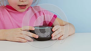 Kid girl talking to smart speaker and give it orders Little child using smart speaker at home while doing homework.