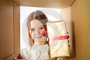 kid girl, teenager, unpacking and opening carton box, and looking inside with surprise