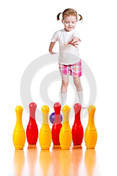 Kid girl throwing ball to knock down toy bowling pins.