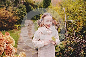 Kid girl walking in the garden in late october or november and playing with maple leaf. Children exploring nature