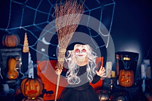 Kid girl in witch costume scaring, making faces with broom in hand on background decor Halloween