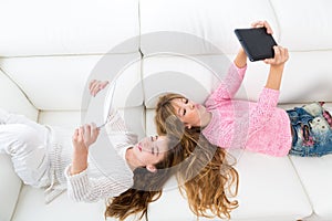 Kid girls having fun playing with tablet pc lying sofa