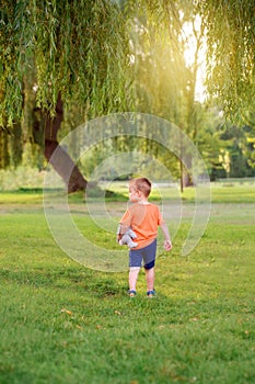 Kid going to future. Little cute toddler Caucasian boy in red orange t-shirt with stuffed plush toy walking alone in park.