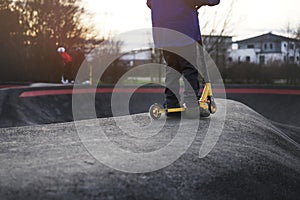 kid with golden stunt scooter stands on elevation in modern asphalted pump track park