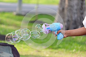 Kid had holds blowing bubble gun for making soap bubbles at green garden. Child having fun with bubble in summer park. Kid