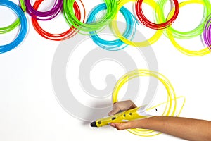 Kid hand with 3d pen and colourful plastic filament on white table background. Top view