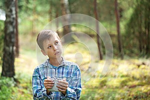 Kid hand holding bowl of freshly picked wild blueberries against bokeh green forest background