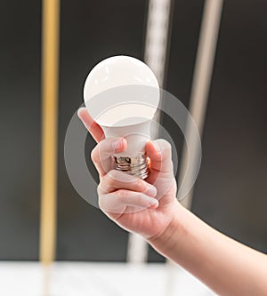 Kid hand holding brand new white LED light bulb against wooden background