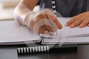 Kid hand learning, writing school homework on paper notebook. Close up