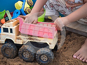 Kid hand playing car truck toy on sand background.