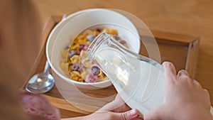 kid hand pouring fresh milk on the white cup, cornflakes cereal, strawberry, blackberry and milk in a white bowl, selective focus