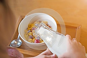 kid hand pouring fresh milk on the white cup, cornflakes cereal, strawberry, blackberry and milk in a white bowl, selective focus