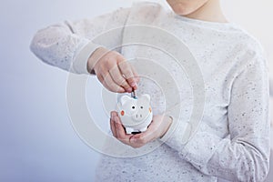 Kid hand putting coin into piggy bank or money box.