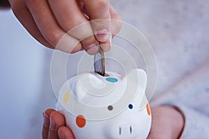 Kid hand putting coin into piggy bank or money box.