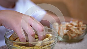 Kid hand takes chips, crackers from a plate. Dining with harmful snack foods