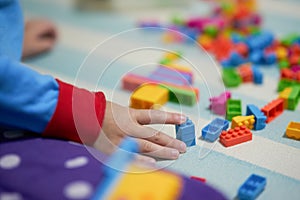 Kid hand touch colorful bricks toy on mat floor for playing