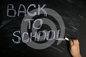 Kid hand write message back to school with white chalk on black chalkboard