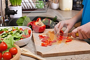 Kid hands chopping red bellpepper for a delicious vegetable salad photo