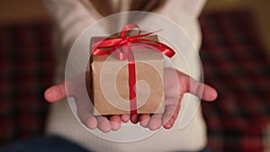 Kid hands holding Christmas gift box with red ribbon. Child giving small present