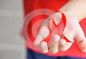 Kid hands holding red AIDS awareness ribbon.