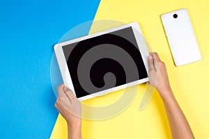 Kid hands holding tablet computer on blue and yellow background
