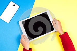 Kid hands holding tablet computer on blue and yellow background