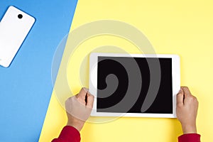 Kid hands holding tablet computer on blue and yellow background