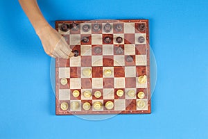 Kid hands over a chessboard playing chess game on blue background, top view