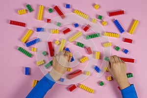 Kid hands playing with colorful building plastic bricks on pink background. Educational developing toys background