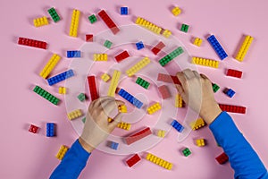 Kid hands playing with colorful building plastic bricks on pink background. Educational developing toys background