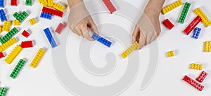 Kid hands playing with colorful building plastic bricks on white background. Educational developing toys background