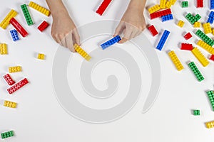 Kid hands playing with colorful building plastic bricks on white background. Educational developing toys background