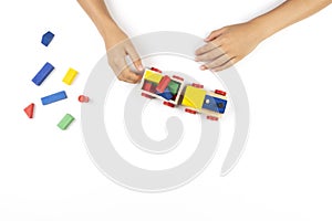 Kid hands playing with toy train and colorful wooden cube blocks on white table background. Top view