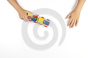 Kid hands playing with wooden toy train on white table background. Top view