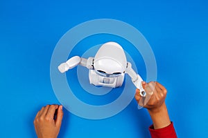 Kid hands with toy robot on blue background.