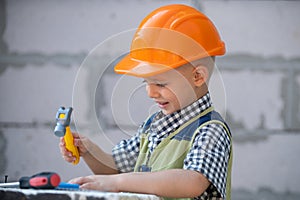 Kid in hard hat holding hammer. Little child helping with toy tools on construciton site. Kids with construction tools