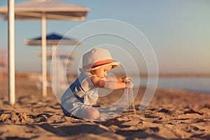 Kid in a hat playing with sand on the beach by the sea. holidays with children near the ocean