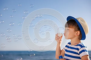 Kid having fun on the beach. Boy blowing soap bubbles